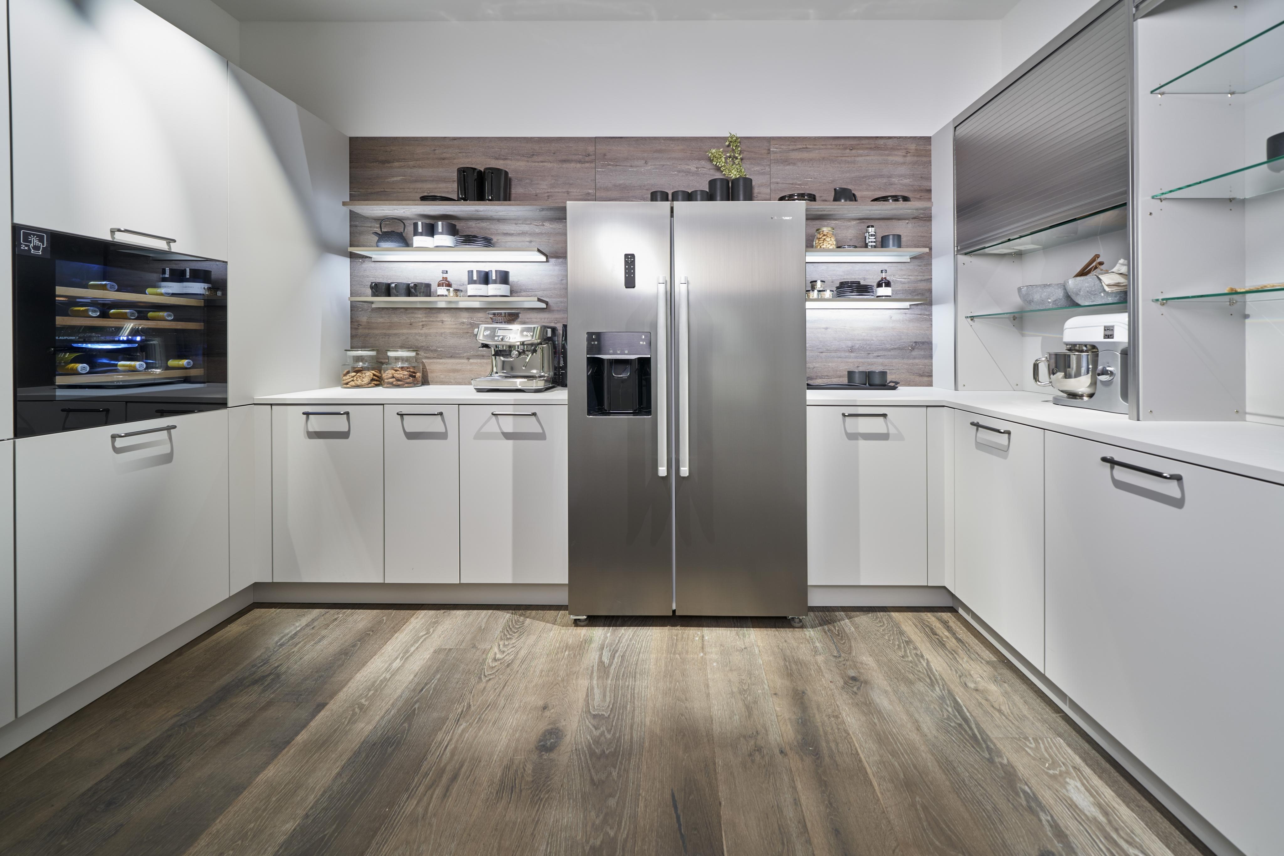 weiße U-Küche mit Regalen und einer Holzarbeitsplatte, in der Mitte mit Side by Side Kühlschrank