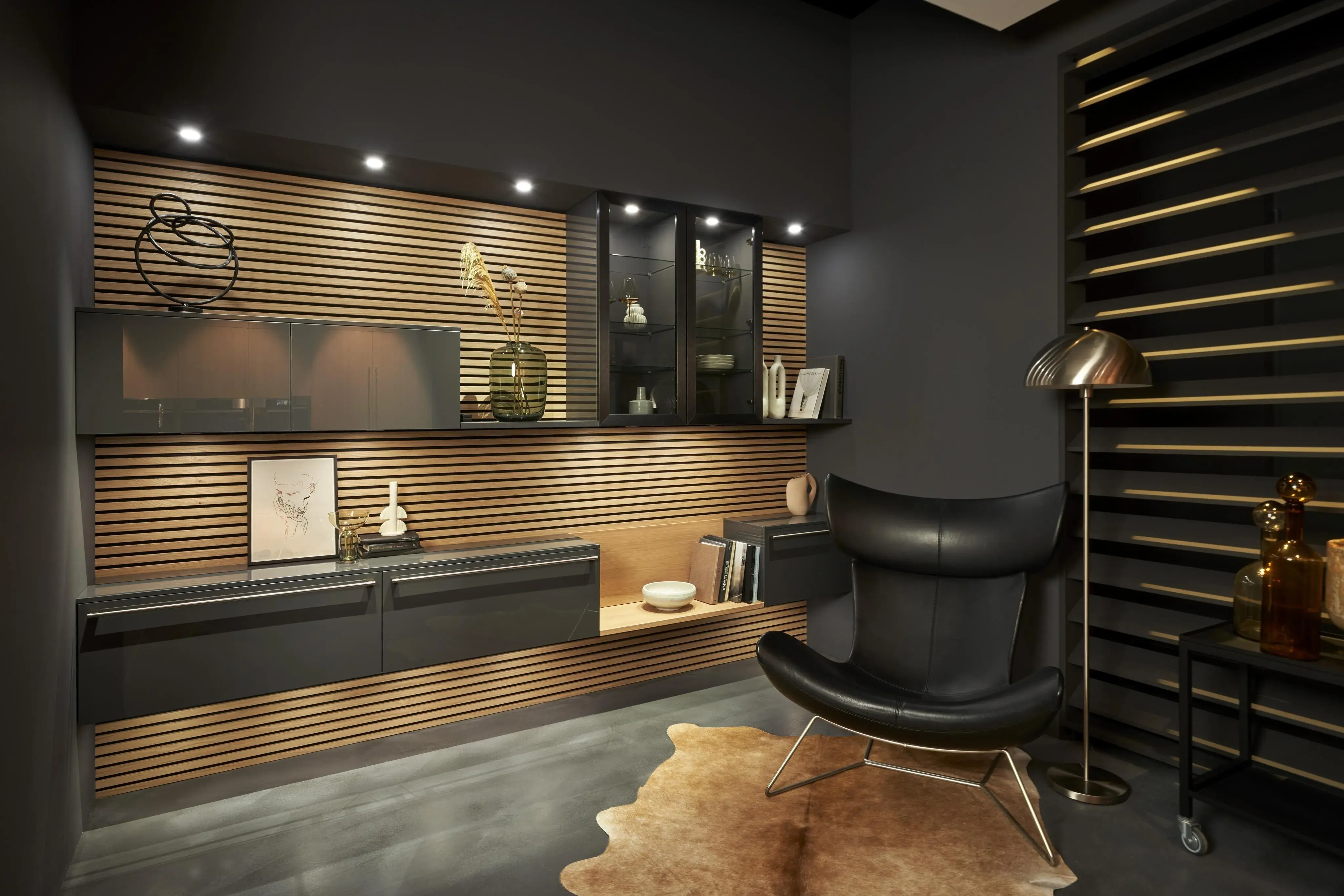 Holzrückwand mit schwarzen Schrankelementen, eins davon mit Glas